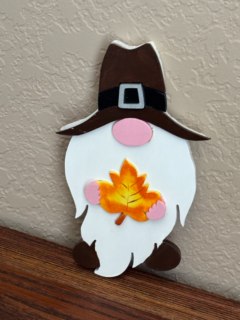 Decorative gnome with a brown hat and leaf on a neutral background