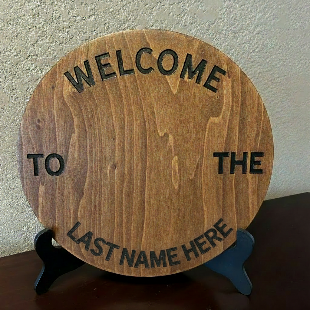 Hand-painted 12-inch customizable birch round with Welcome to the Last Name Here text, displayed on a black easel stand, handcrafted wood home decor