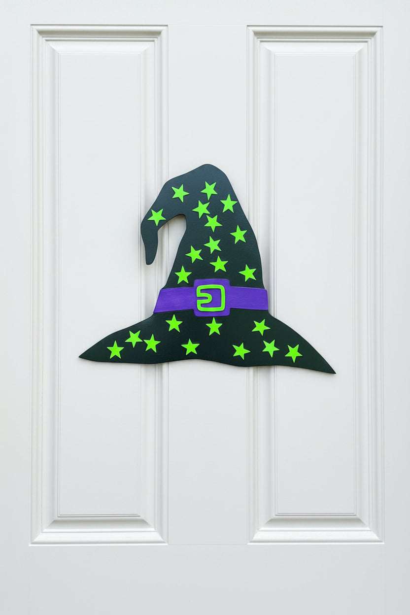 Witch hat decoration with green stars and a purple buckle on a beige door.