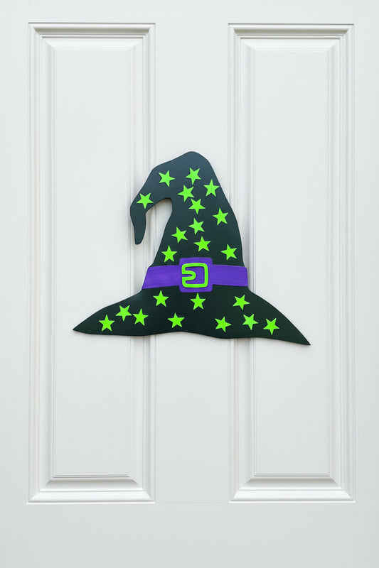 Witch hat decoration with green stars and a purple buckle on a beige door.